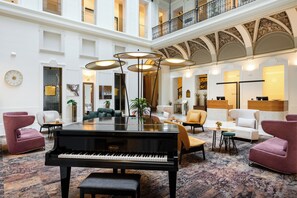 A grand lobby with a grand piano, plush seating, and a high ceiling with ornate detailing.