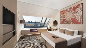 A modern hotel room with a large bed, a desk, a chair, a TV, and a window with a city view.