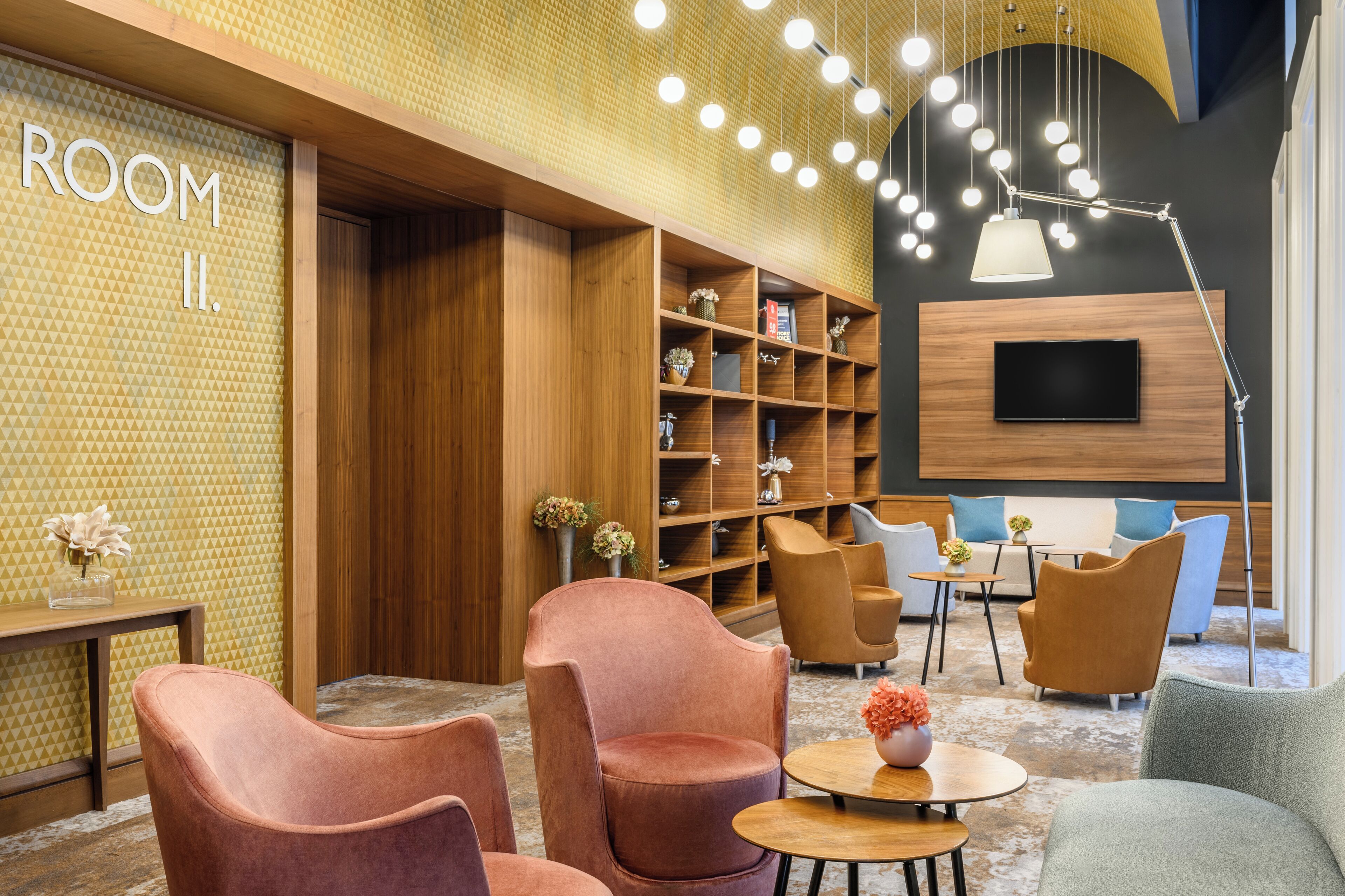 A modern lobby with a wooden bookshelf, seating area, and a TV mounted on the wall.