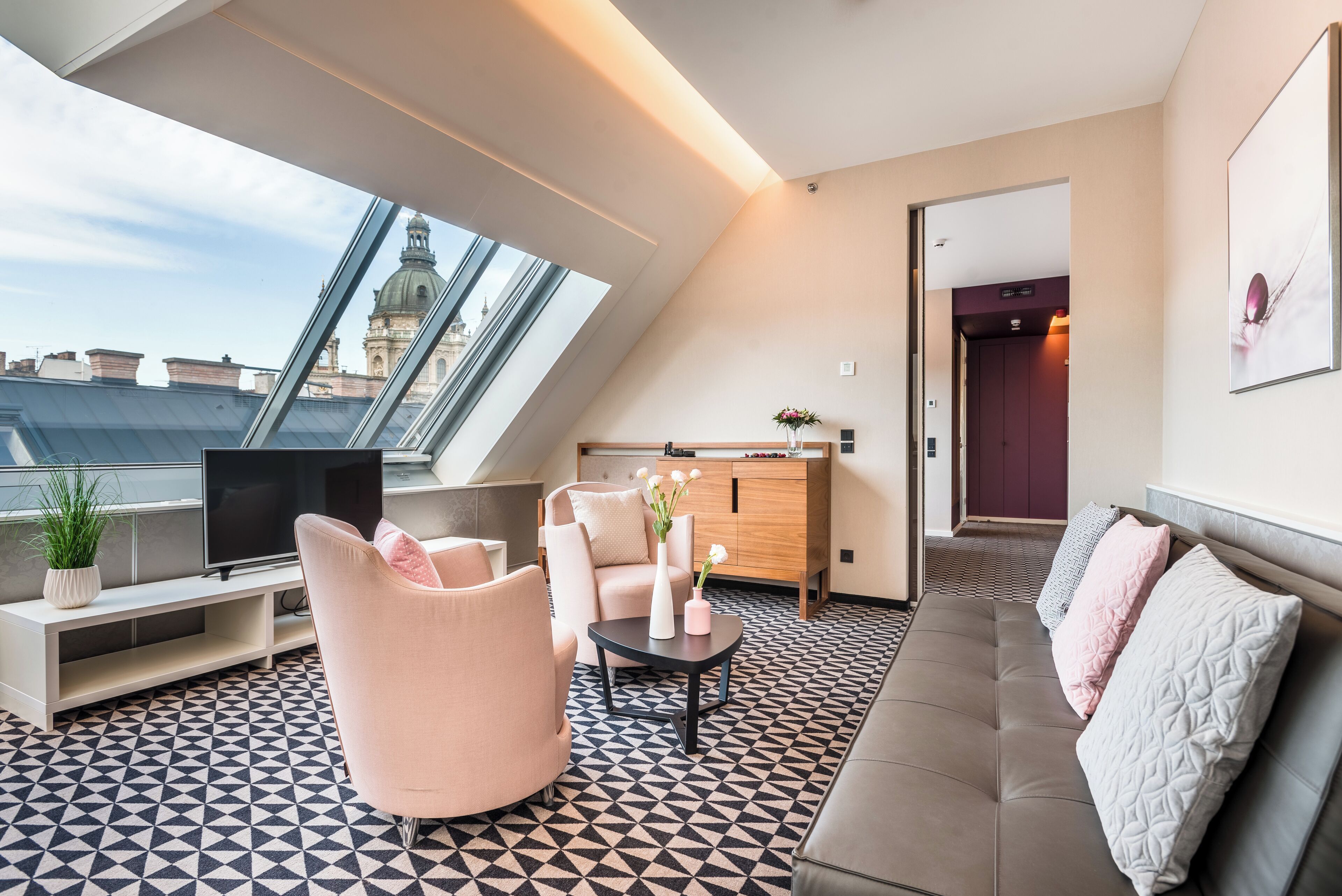 Una sala moderna con televisor, sofá y sillones, un mueble de madera y un ventanal con vistas a la ciudad.