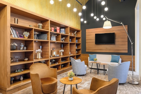 A modern interior with a large wooden bookshelf, a flat-screen TV mounted on the wall, and contemporary seating arrangements.