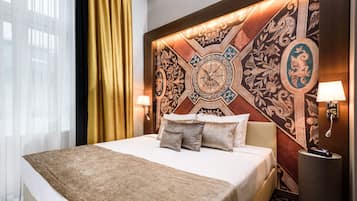 A hotel room with a large bed, a decorative headboard, a nightstand with a lamp, and a window with sheer curtains.
