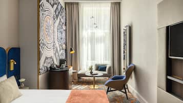 A hotel room with a bed, a desk, a chair, a small table, and a TV.