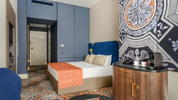 A hotel room with a bed, a desk with a coffee maker, a tray of snacks, and a decorative wall.