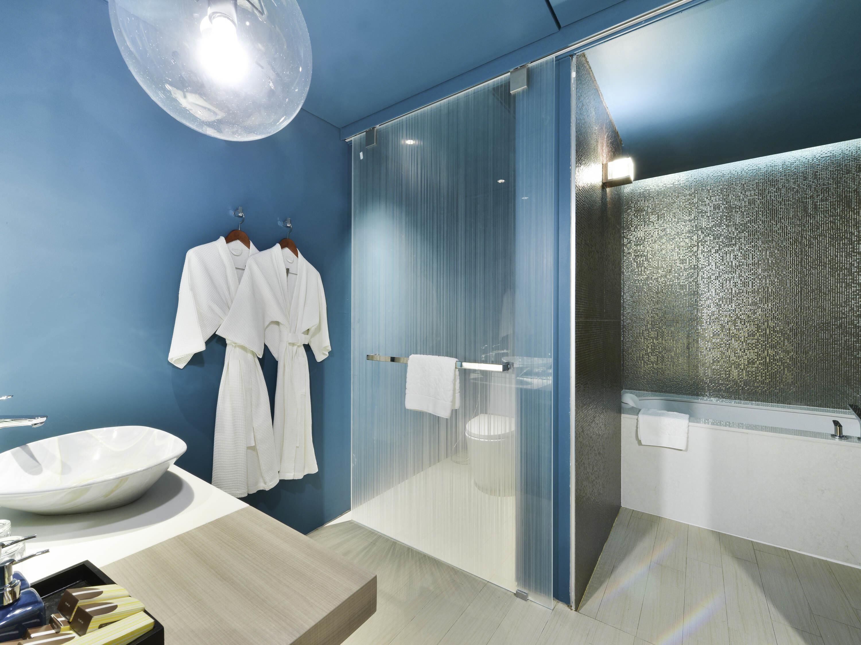 Une salle de bain moderne avec un grand miroir, une douche en verre et un lavabo blanc.