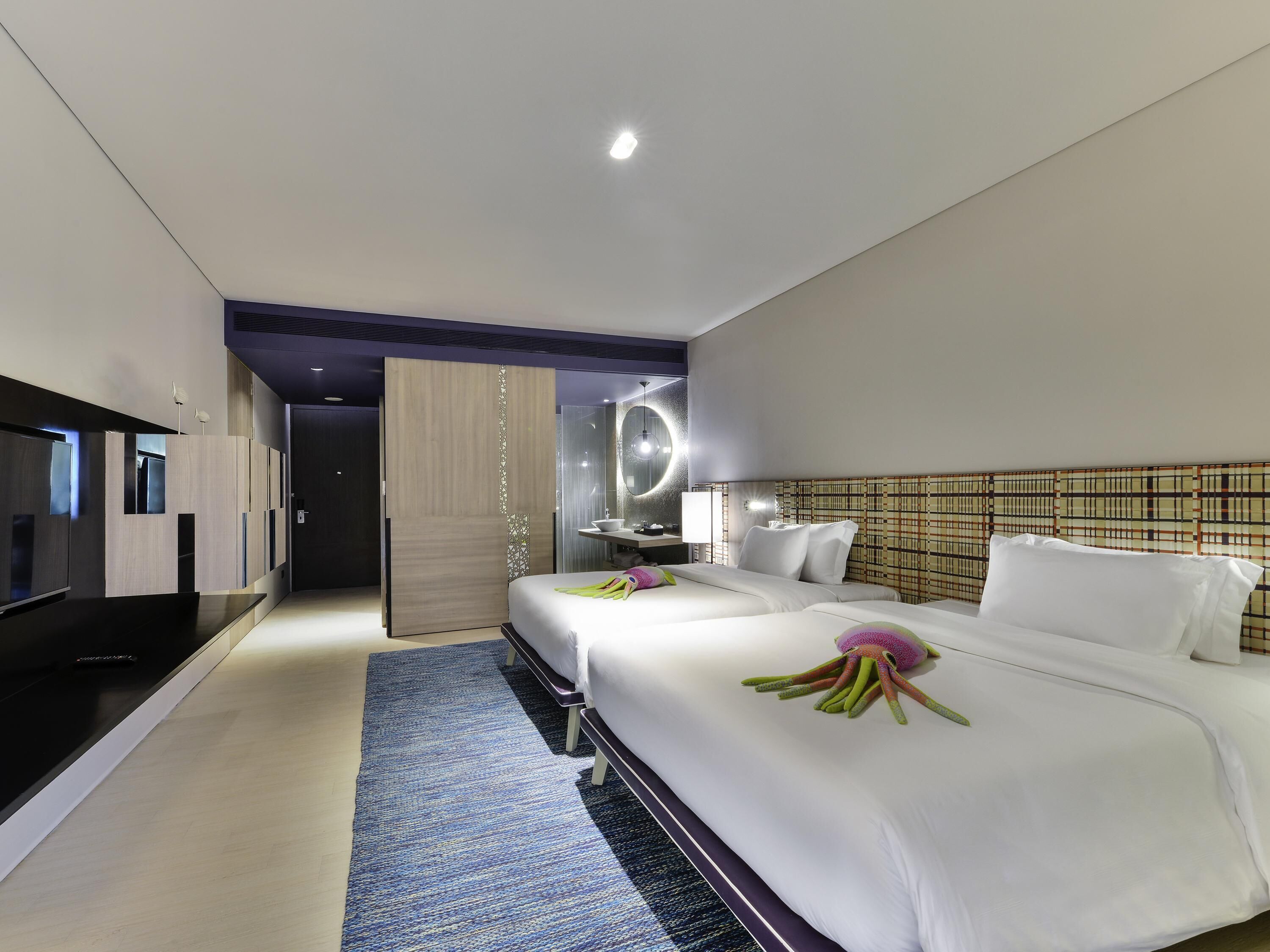 Une chambre d’hôtel moderne dotée d’un grand lit, d’une télévision à écran plat, d’une salle de bain avec un miroir et d’une armoire en bois.