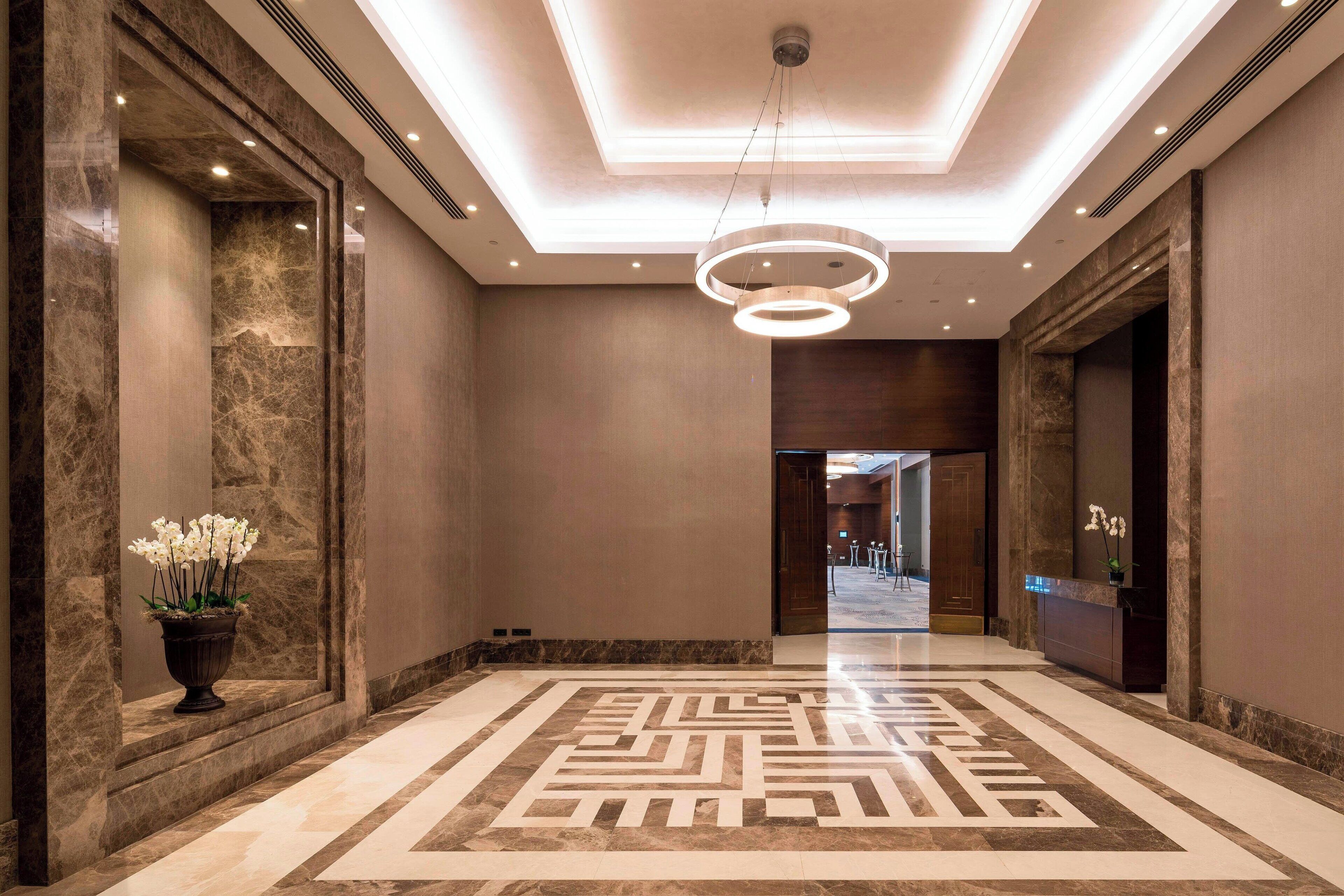 A spacious hallway with marble flooring, a modern chandelier, and a reception desk.