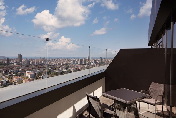 A balcony with a table and chairs, overlooking a cityscape with buildings and a clear sky.