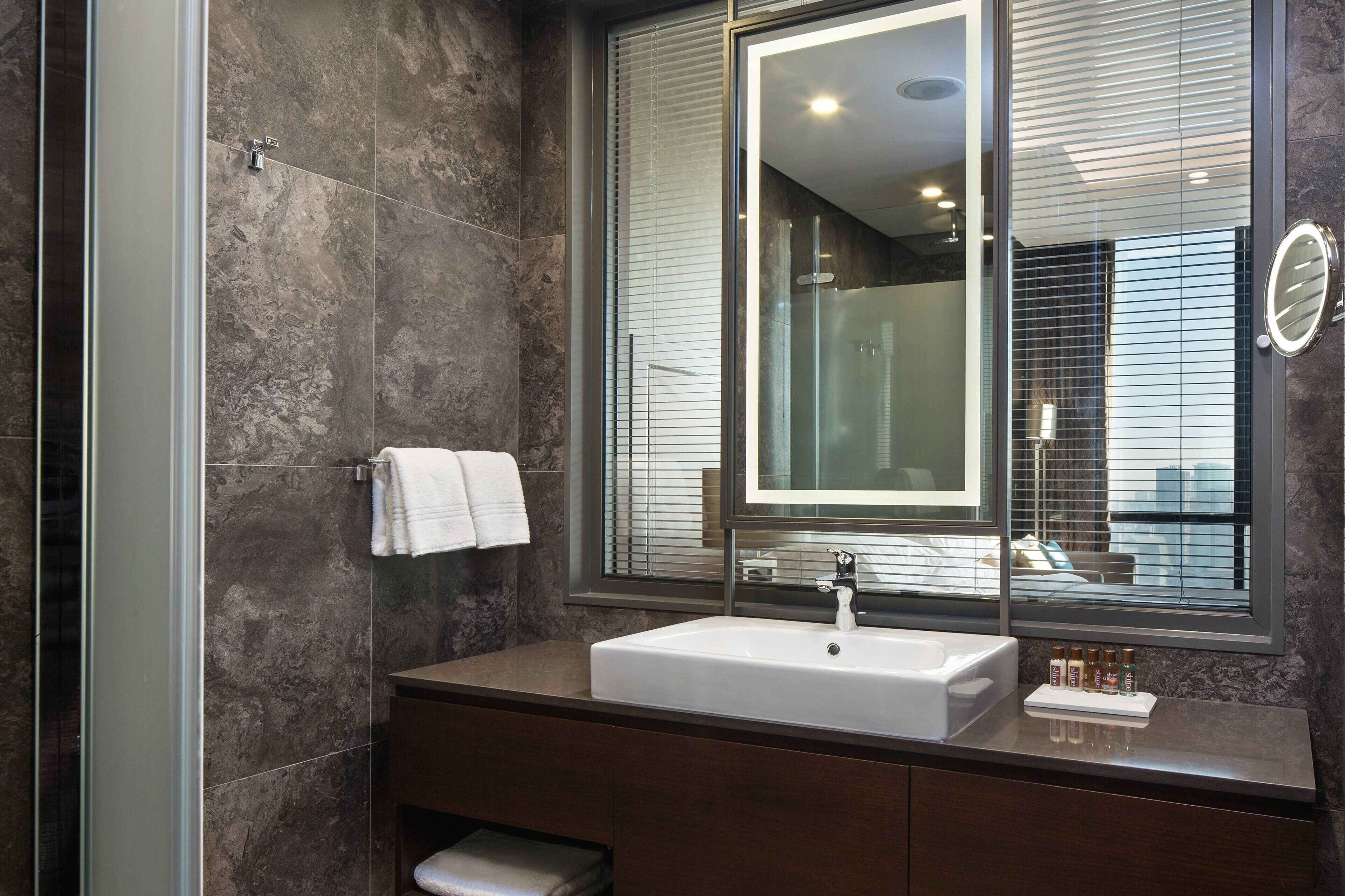A modern bathroom with a large mirror, a white sink, and a vanity with toiletries.