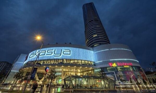 Un edificio moderno con un llamativo letrero 'Akasiya', una zona de juegos KidZania y un rascacielos alto contiguo.
