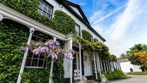 A white building with green ivy and purple flowers, a stone lion statue, and a clear sky. - Statham Lodge Hotel (Lymm)