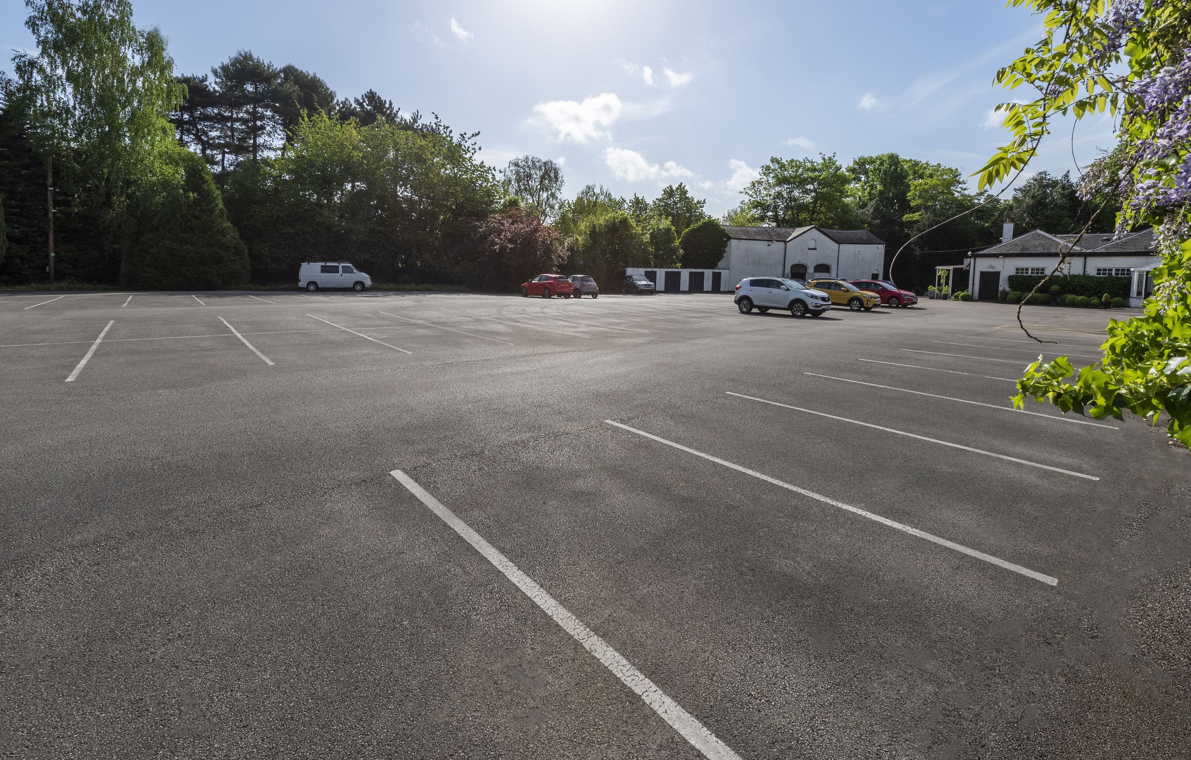 A parking lot with several cars, trees, and buildings in the background.