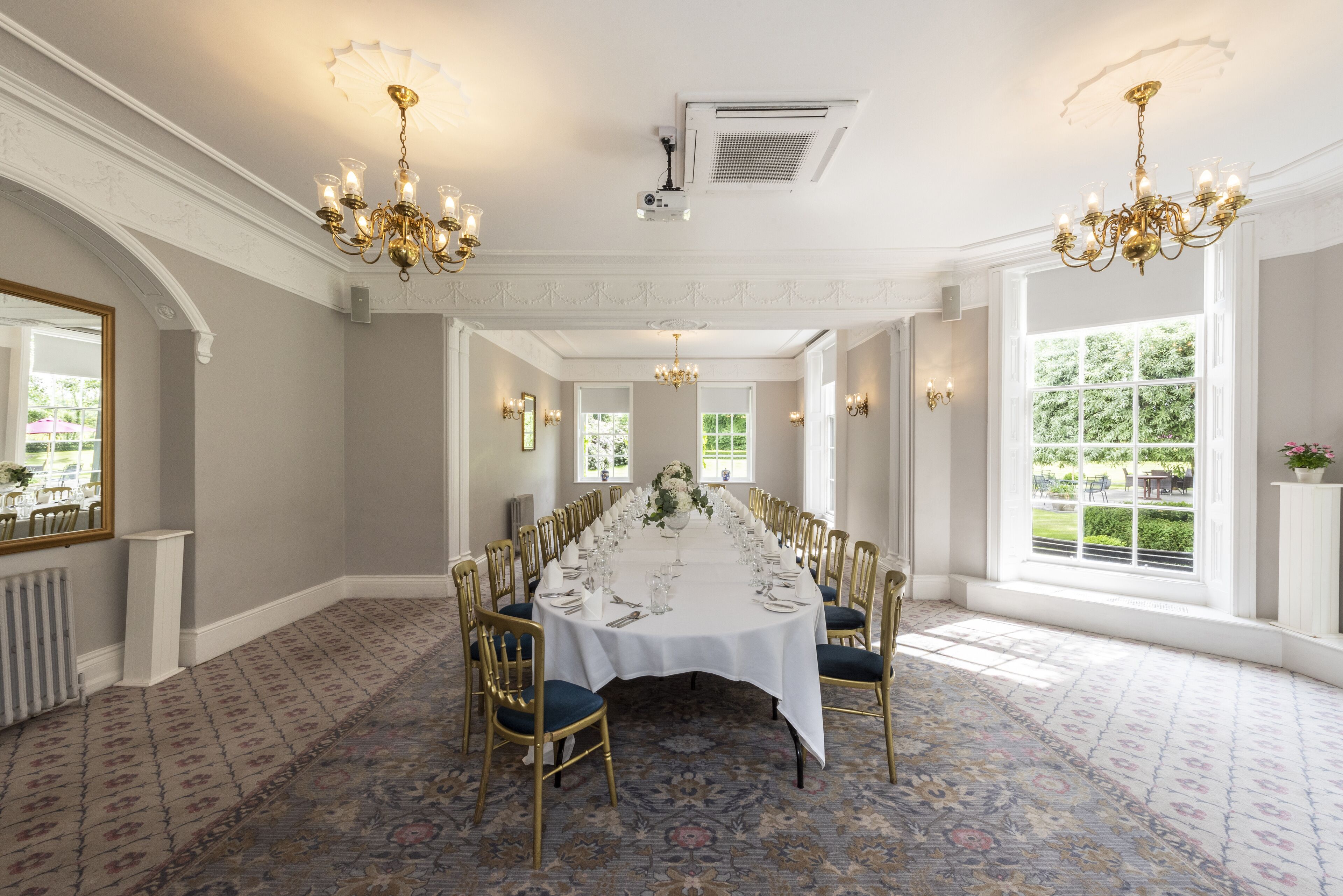 A formal dining room with a long table set for a meal, surrounded by gold chairs, and adorned with chandeliers.