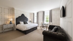 A hotel room with a large bed, a dark headboard, a small table with chairs, and a TV mounted on the wall. - Statham Lodge Hotel (Lymm)