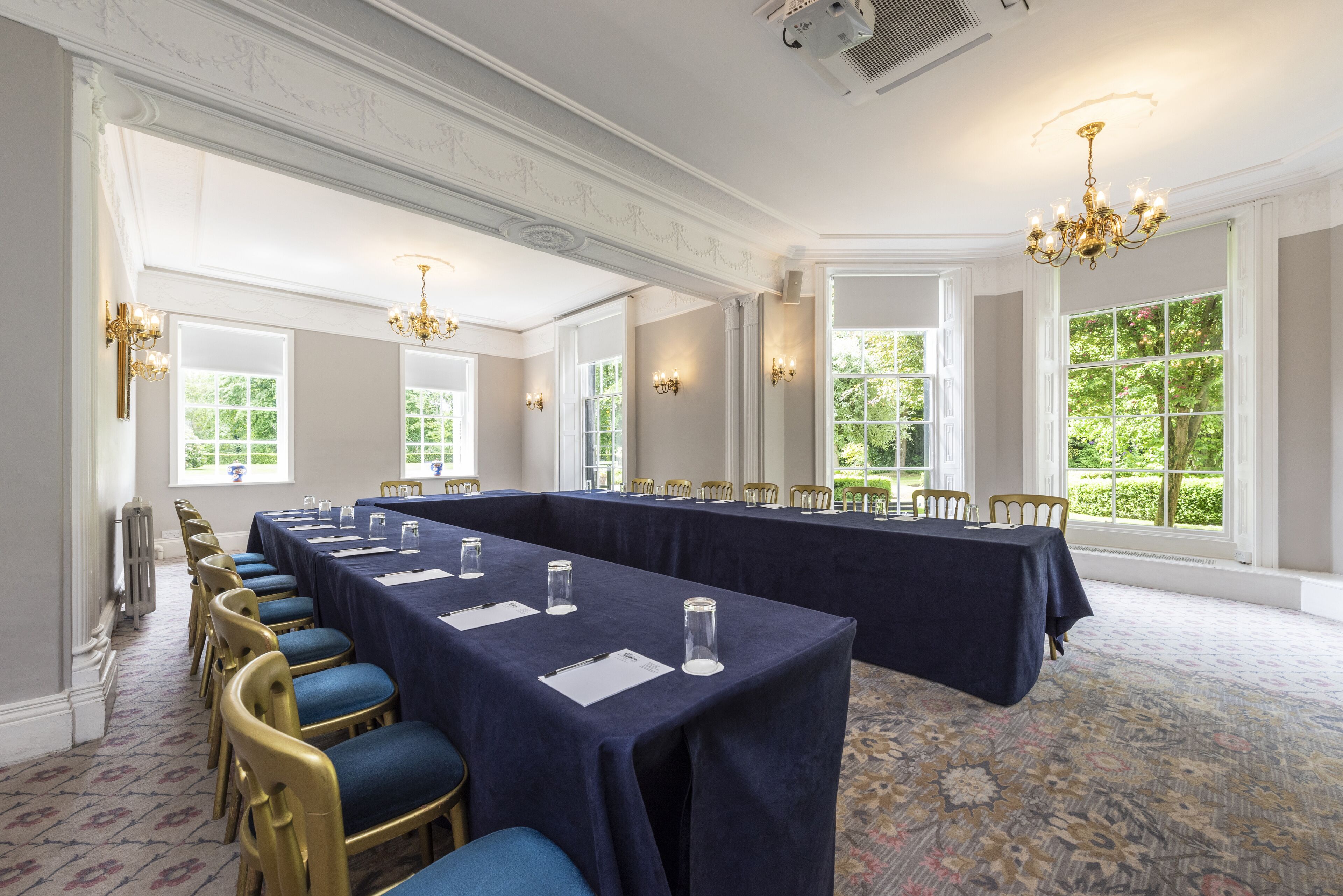A conference room with long tables, chairs, and chandeliers.