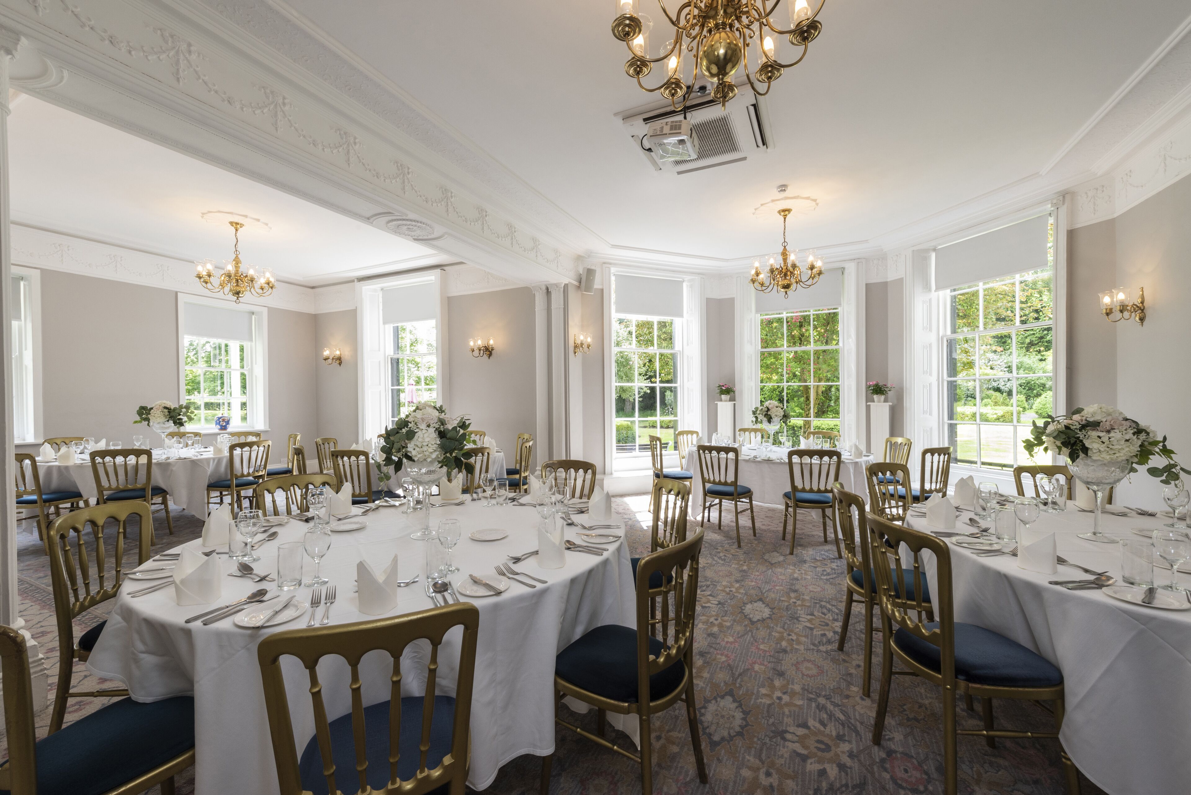 Een stijlvolle eetzaal met ronde tafels, gouden stoelen en kroonluchters.
