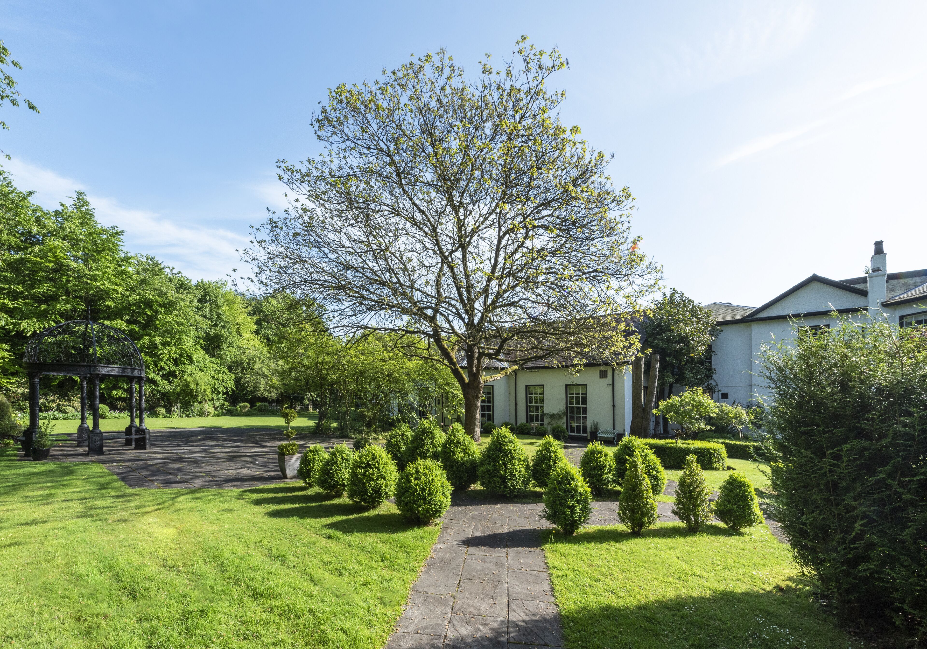 A well-maintained garden with a gazebo, a pathway, and neatly trimmed bushes.