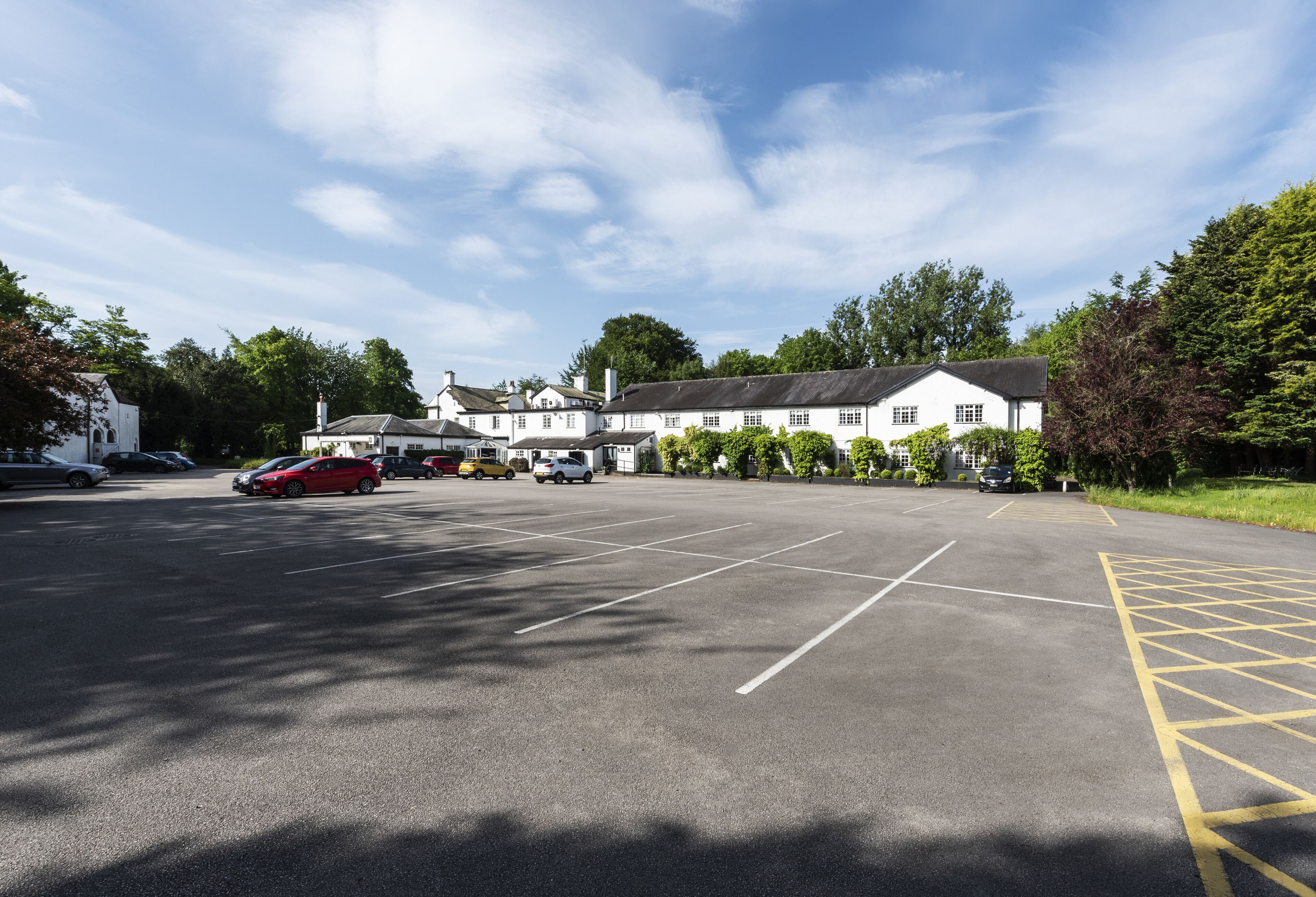 A parking lot with several cars, a building with multiple windows, and trees in the background.