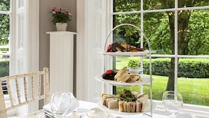 A table set for a tea service with a tiered dessert display, salt and sugar shakers, a teapot, and a floral-patterned pitcher. - Statham Lodge Hotel (Lymm)