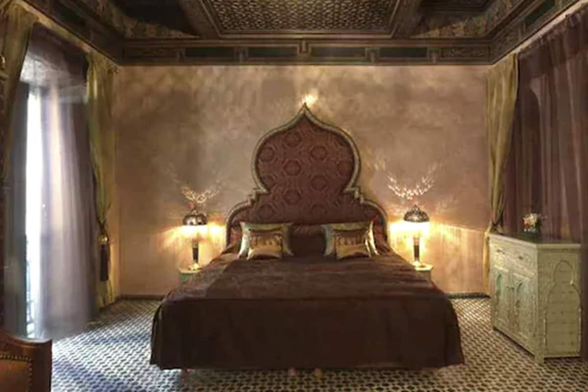 A bedroom with a large bed, two bedside lamps, a decorative ceiling, and a nightstand.