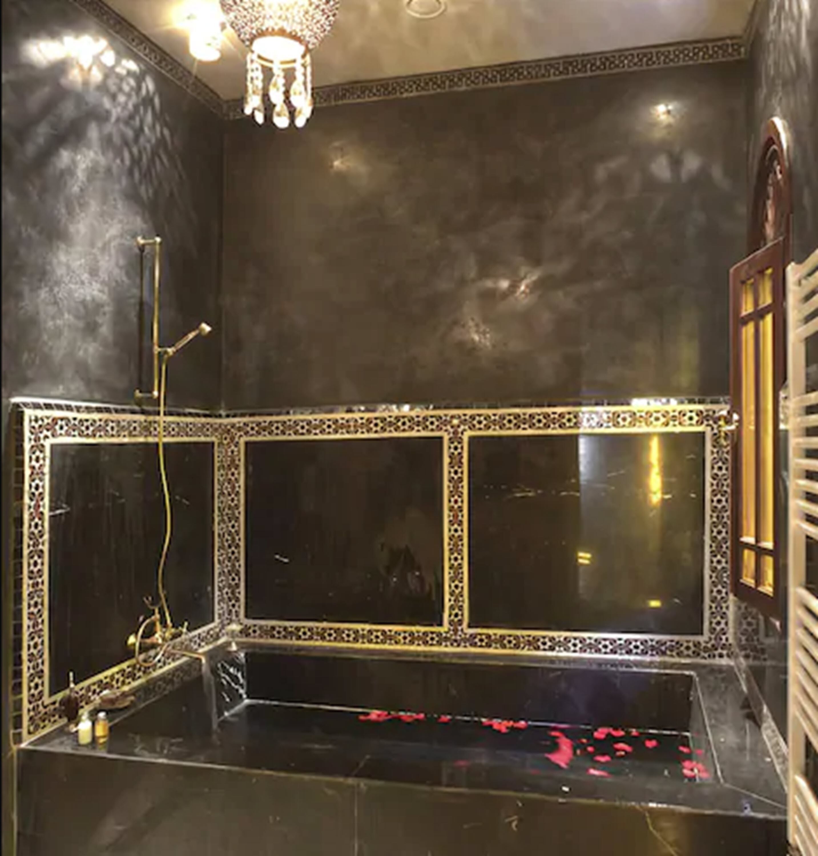 Un baño con un espejo grande, una bañera con pétalos de rosa y un candelabro.