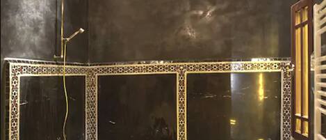 Un baño con un espejo grande, una bañera con pétalos de rosa y un candelabro.
