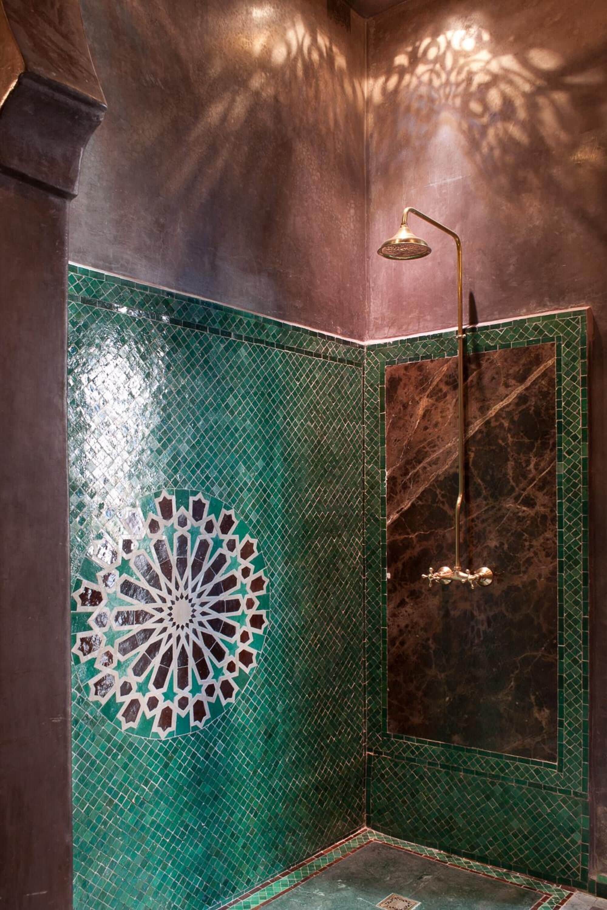 A shower with a gold showerhead and a green mosaic tile wall.