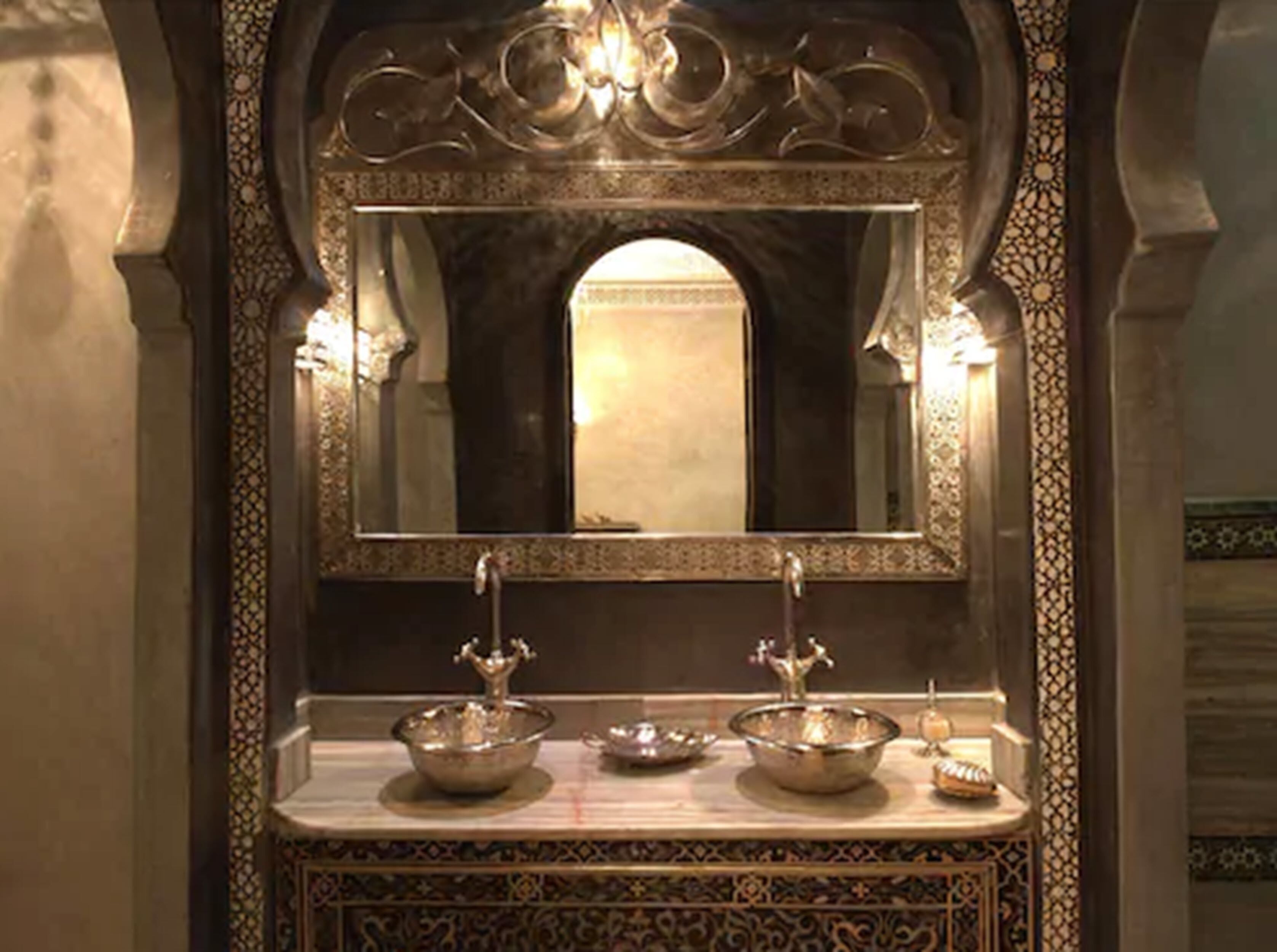 Un baño ornamentado con un espejo grande, dos lavamanos e iluminación decorativa.