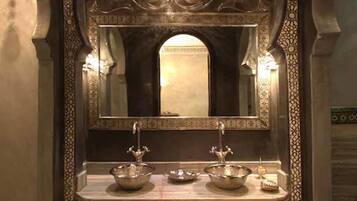 Un baño ornamentado con un espejo grande, dos lavamanos e iluminación decorativa.