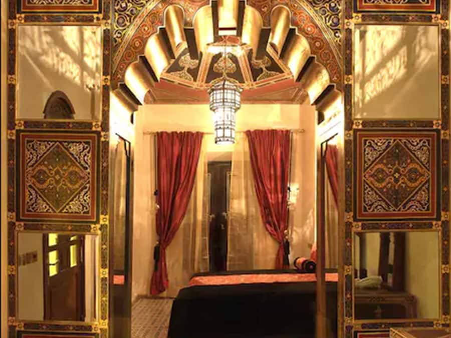 Une pièce avec un sol à motifs, un lit recouvert d’une couverture rouge et des décorations murales élaborées.