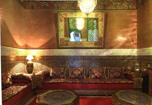 A richly decorated room with a sofa set, ornate wall patterns, and a chandelier.