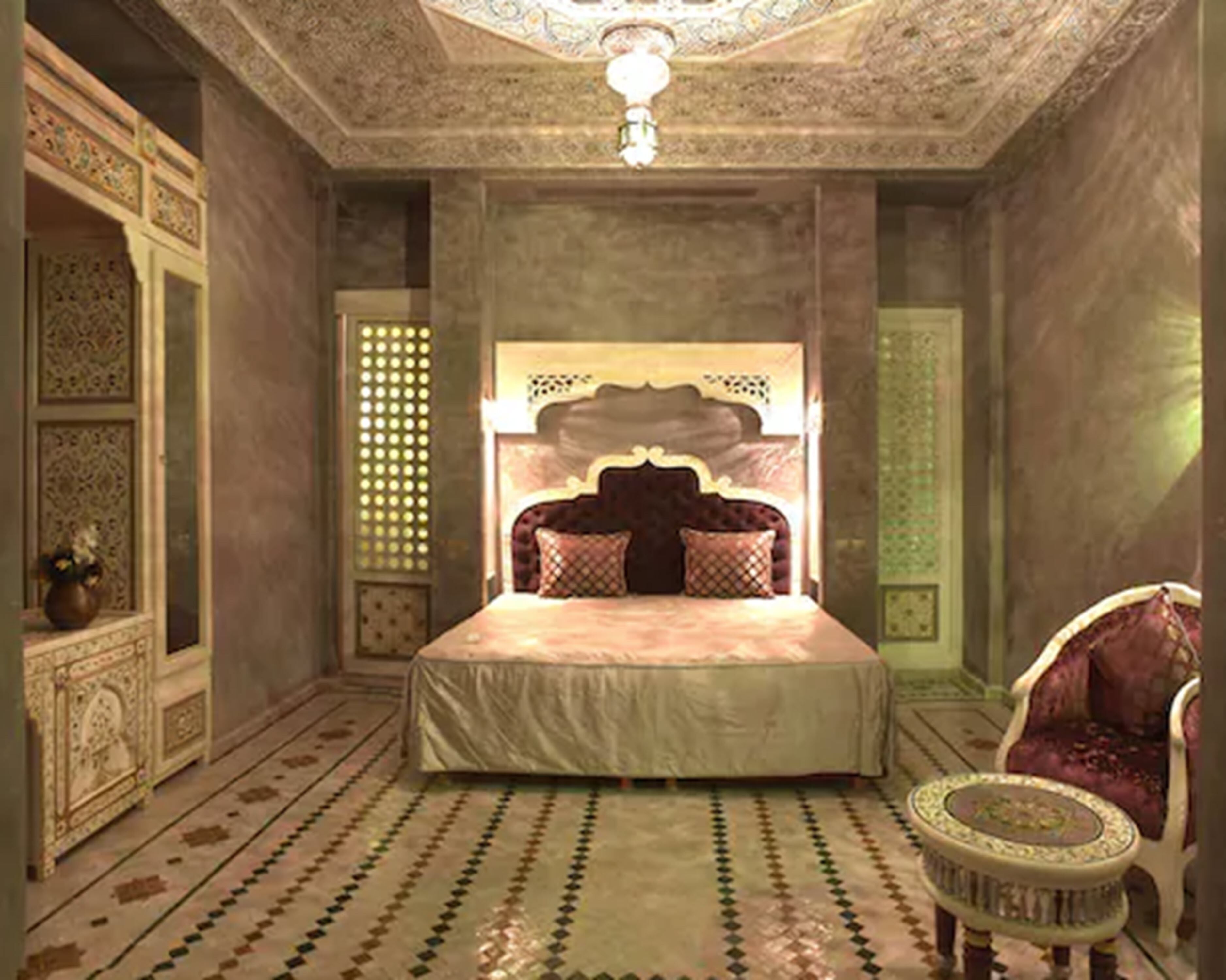 Un dormitorio con una cama grande, un cabecero ornamentado, alfombra estampada y una silla decorativa.