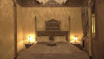 A large, ornate bed with a high headboard, flanked by two bedside tables with lamps, in a room with patterned walls and a decorative ceiling.