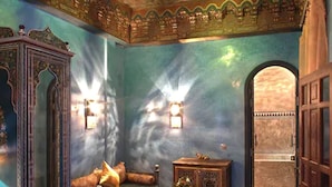 A room with a patterned floor, a bed with pillows, a nightstand with a lamp, and a decorative mirror. - Riad Mumtaz Mahal (Essaouira)