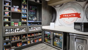 A snack bar with shelves stocked with various snacks and drinks, a chalkboard with a positive message, and a sign indicating the availability of treats. - Hampton Inn & Suites Ardmore (Ardmore)
