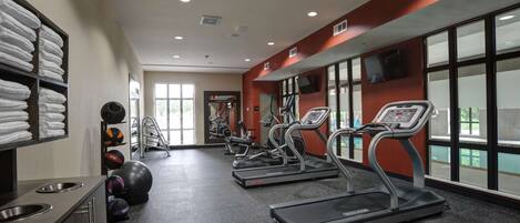 Een sportschool met loopbanden, fitnessballen en een televisie aan de muur.