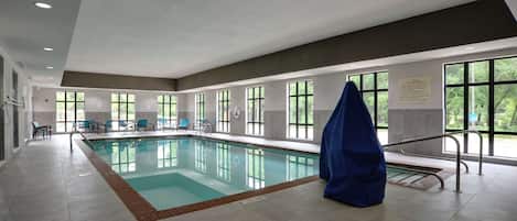 An indoor swimming pool with clear windows, a covered bench, and a safety sign.