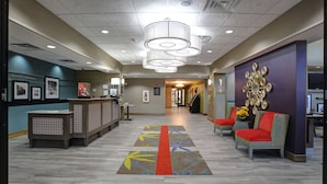 A reception area with a counter, chairs, a patterned carpet, and a wall with framed pictures. - Hampton Inn & Suites Ardmore (Ardmore)