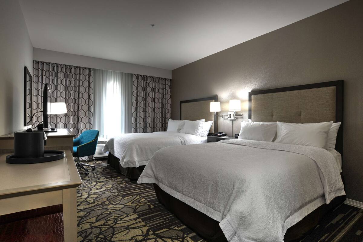 A hotel room with two beds, a desk, a chair, and a patterned carpet.