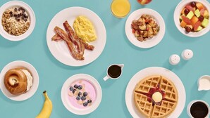 A breakfast spread with various dishes including bacon, scrambled eggs, waffles, and fruit.