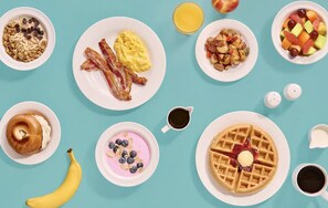 A breakfast spread with various dishes including bacon, scrambled eggs, waffles, and fruit.