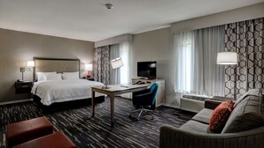 A hotel room with a bed, desk, chair, and sofa.