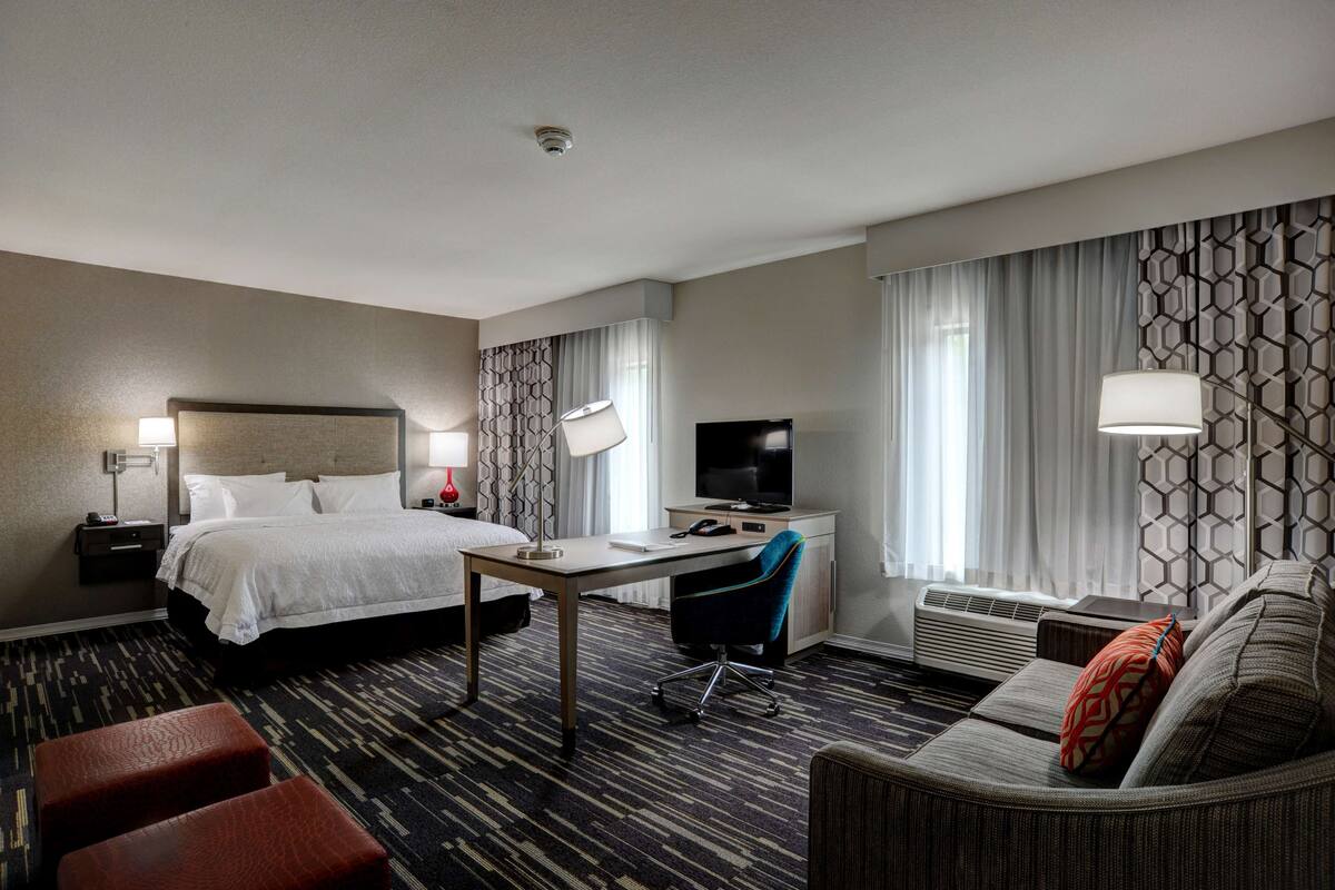 A hotel room with a bed, desk, chair, and sofa.