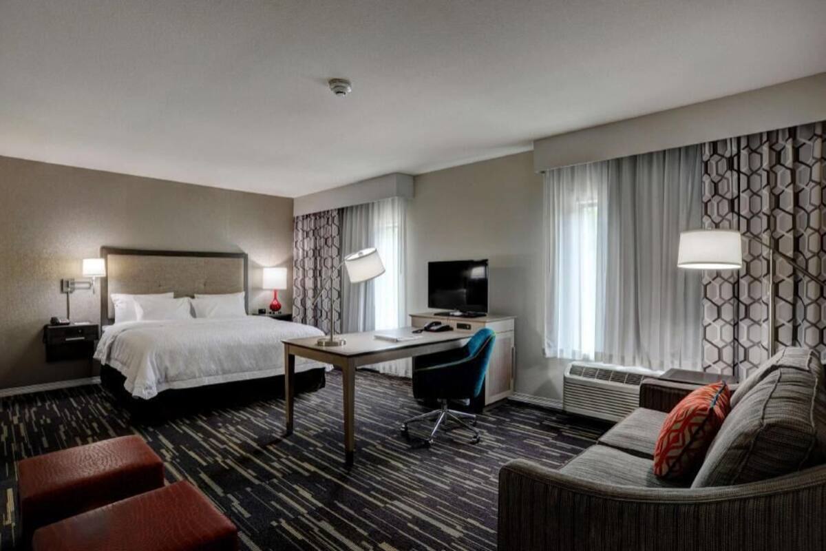 A hotel room with a bed, desk, chair, sofa, and a television.
