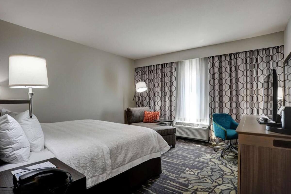 A hotel room with a bed, desk, chair, and a patterned curtain.