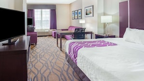 A hotel room with a bed, a desk, a chair, a television, a sofa, and a window with curtains. - La Quinta Inn & Suites by Wyndham Luling (Luling)