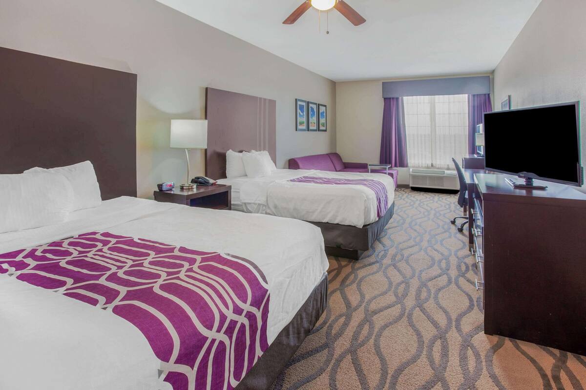 A hotel room with two beds, a desk, a television, and a window with curtains.