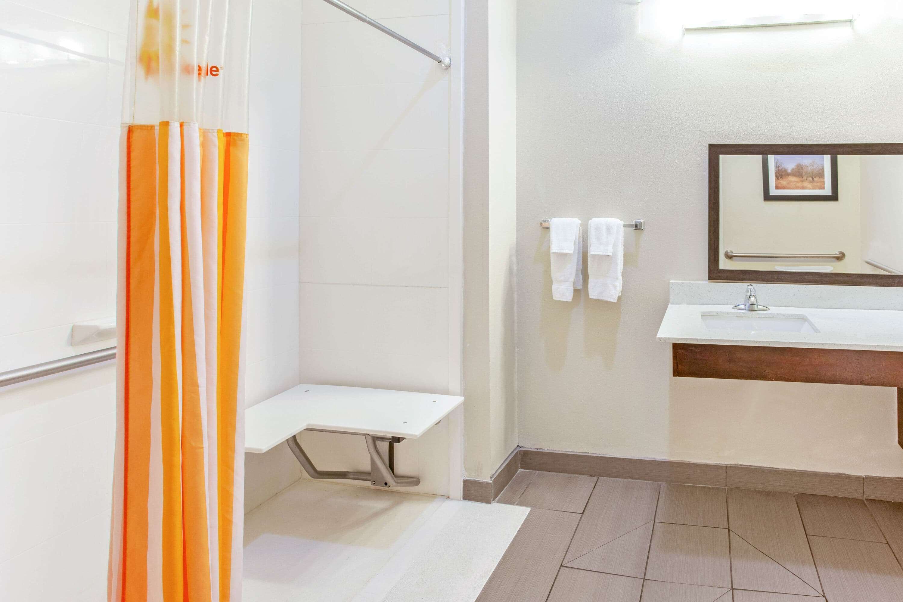 Une salle de bain avec une douche, un lavabo, un miroir et un banc.