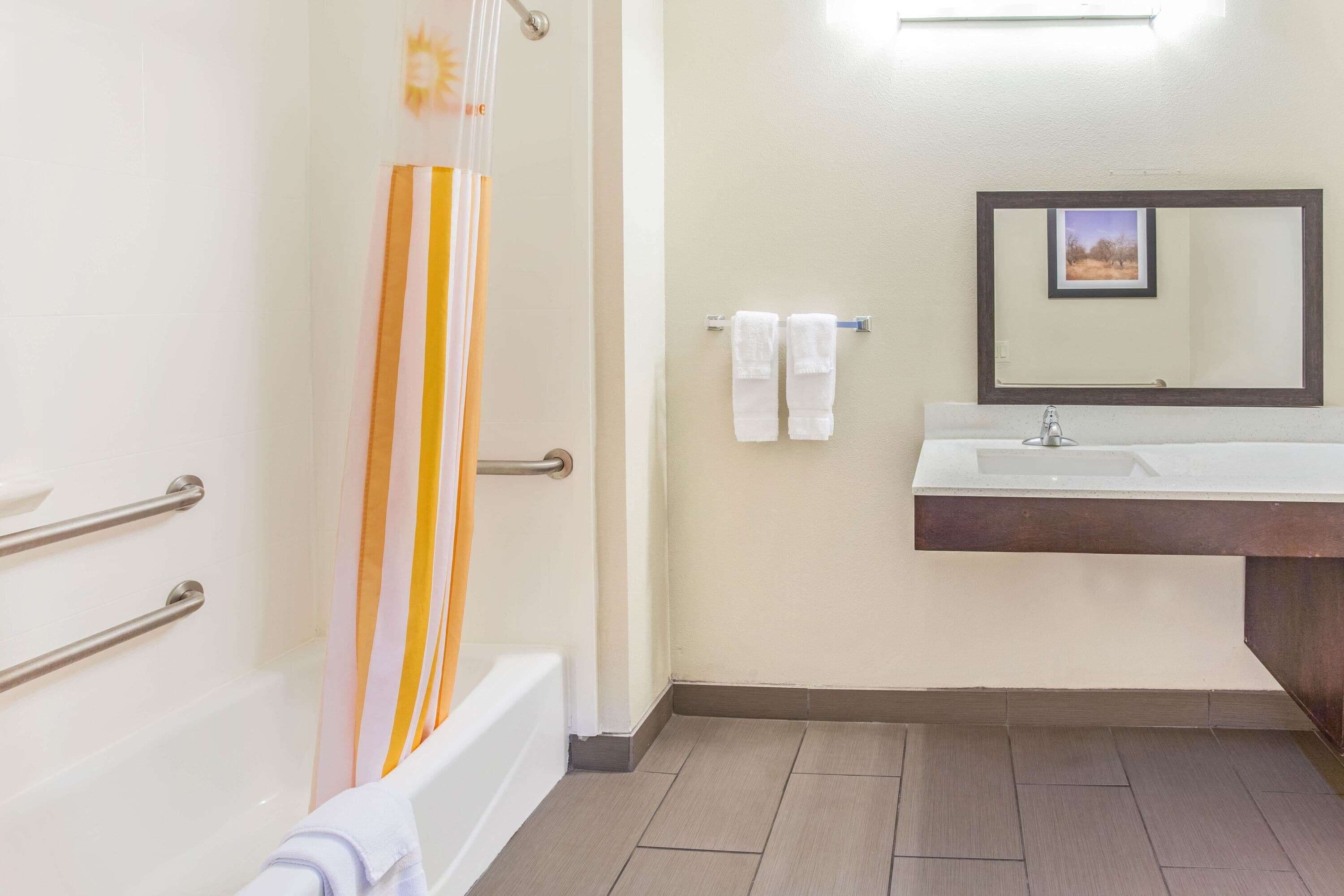 A bathroom with a bathtub, a shower curtain, a sink with a mirror, and two towels on a rack.