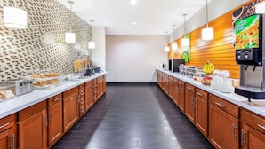 A modern kitchen with a long counter, wooden cabinets, and a tiled backsplash. - La Quinta Inn & Suites by Wyndham Luling (Luling)